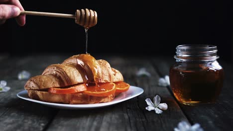 Slow-motion-footage-of-honey-dripping-onto-a-croissant-filled-with-three-orange-slices