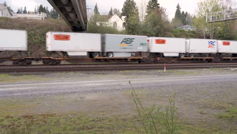 Train-of-flatbed-cars-carrying-truck-containers-travels-beneath-underpass