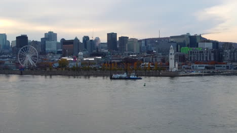 Boat-sailing-on-saint-Laurent-river,-old-port,-Montreal,-Quebec,-Canada,-ferris-wheel,-tower,-buildings,-downtown-Montreal,-cityscape,-skyline-aerial-view-by-drone