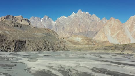 slow-moving-aerial-drone-panning-up-from-the-river-and-revealing-Passu-Cones-mountains-in-Hunza-Pakistan-next-to-the-famous-Hussaini-Bridge
