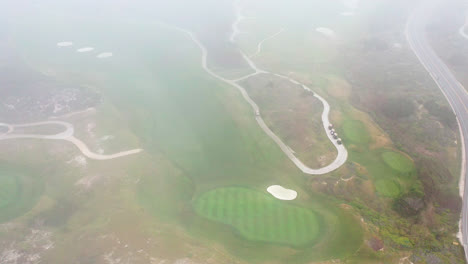 Cinematic-aerial-view-of-golf-course-revealed-through-fog