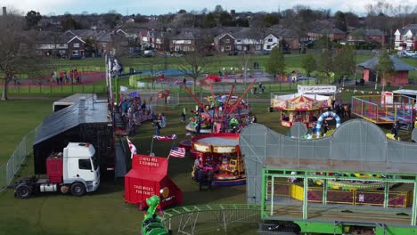 Small-town-fairground-Easter-holidays-funfair-rides-in-public-park-aerial-view-tilt-up-left