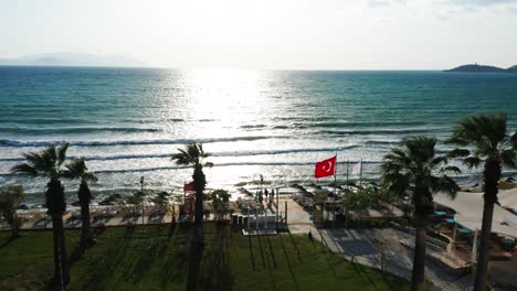 Turkish-flag-is-waving-in-wind-on-sandy-beach,-famous-tourist-destination-in-Kusadasi