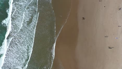 Top-down-aerial-shot-of-a-warm-tropical-beach-with-waves-gently-crashing-onto-the-shore