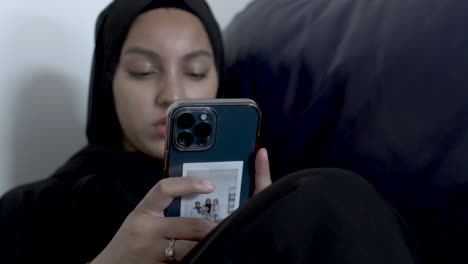 Hintergrund-Verschwommene-Sicht-Auf-Junge-Muslimische-Frauen,-Die-Hijab-Tragen-Und-Auf-Dem-Smartphone-Tippen,-Während-Sie-Auf-Dem-Sofa-Sitzen