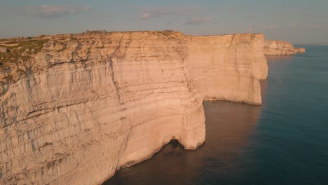 Impresionantes-Acantilados-De-Piedra-Caliza-De-Malta-Se-Reflejan-En-El-Agua-Del-Mar-Mediterráneo-A-Medida-Que-El-Dron-Se-Acerca-A-La-Formación-Geológica