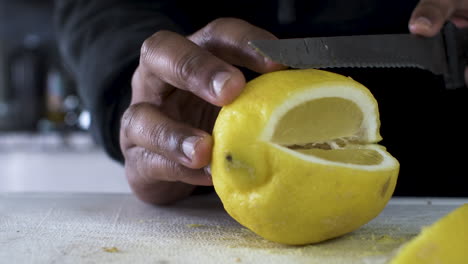 Hand-Of-Ethnic-Minority-Adult-Male-Using-Serrated-Knife-To-Slice-Yellow-Lemon-On-Cutting-Board