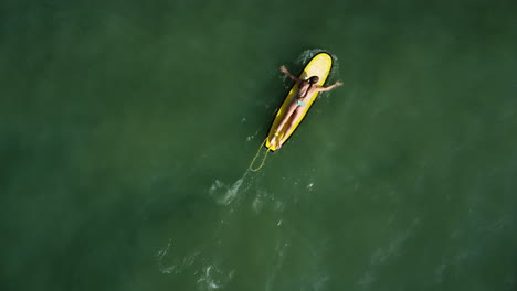 Aerial-top-down,-surfer-girl-paddling-surfboard-on-calm-ocean-water