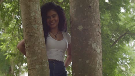 pan-left-of-a-curly-hair-latina-girl-in-the-middle-of-two-tree-trunk-and-smile