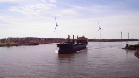 Aerial-Of-Aal-Paris-Cargo-Ship-Approaching-Along-Oude-Maas-With-Still-Wind-Turbines-In-background-In-Barendrecht