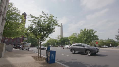 A-side-walk-view-of-the-Washington-Monument-that-slowly-pushes-into-a-street-with-moving-traffic-in-Washington,-DC