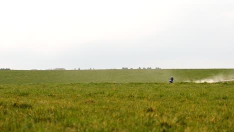 Off-road-motorcyclist-riding-through-frame-in-between-two-green-meadows