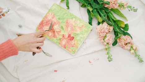 Female-hands-painting-flowers-artwork-with-spatula-next-to-beautiful-flowers