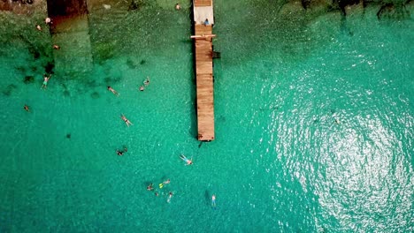 Overhead-jib-up-view-of-people-snorkeling-at-Grandi-Beach-with-fishing-boats-on-shore,-Dutch-island-of-Curacao,-Caribbean-Sea