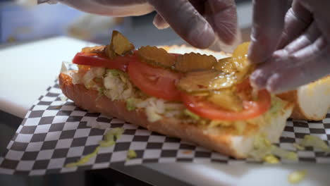 Sandwich-prep,-placing-sliced-dill-pickles-on-crusty-french-bread,-building-a-poboy,-slow-motion-close-up-4K