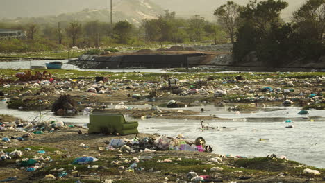 Winding-river-banks-covered-in-plastic-garbage-piles-in-Vietnam,-static-view