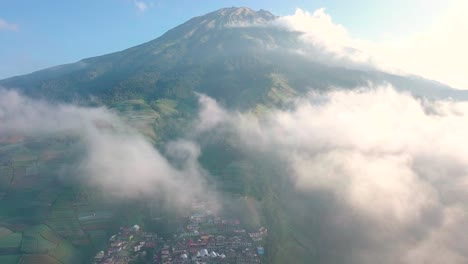 Aerial-drone-flight-through-clouds-revealing-Nepal-Van-Java-Village-and-giant-Mountain-Sumbing-during-sunlight-and-blue-sky-in-Indonesia