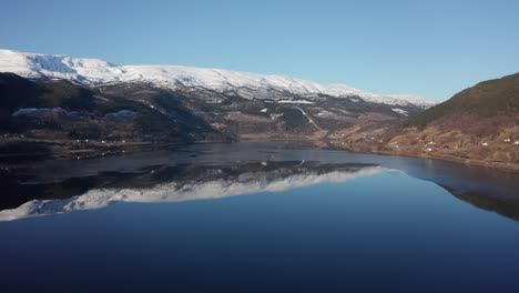Vangsvatnet-lake-in-Vossevangen-shown-with-Bulken-and-Vosso-river-in-background---Aerial-overview-with-snow-capped-mountain-tops