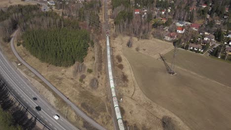 Aerial-view-of-a-long-freight-train-travelling-over-a-road-overpass