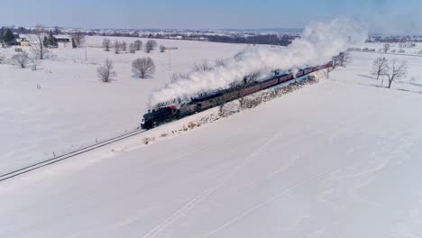 Aerial-View-of-an-Antique-Steam-Locomotive-Approaching-Pulling-Passenger-Cars-and-Blowing-Smoke-and-Steam-After-a-Snow-Storm