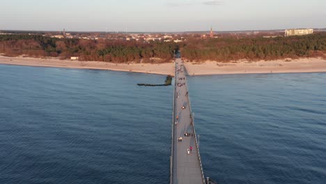 AERIAL:-People-Walking-on-Palanga-Pier-Towards-City-on-Evening-During-Golden-Hour-Time