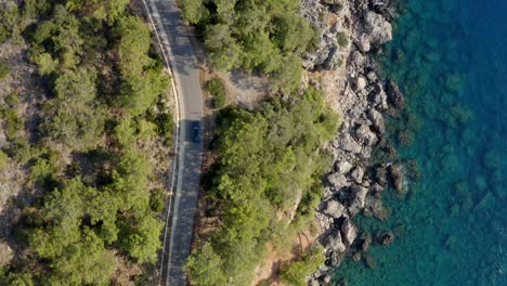 Drone-track-car-driving-on-coastal-highway-by-azure-blue-water