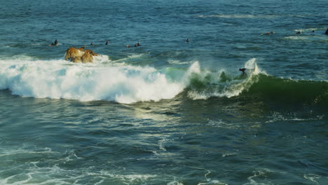 Un-Surfista-Atrapando-Y-Montando-Una-Ola-Mientras-Otros-En-El-Agua-Miran-Frente-A-La-Costa-Del-Sur-De-California