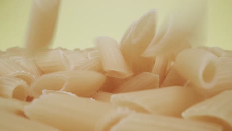 Real-time-probe-close-up-shot-of-falling-mezze-penne-rigate-pasta-on-yellow-background
