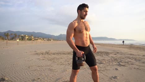 Muskulöser-Mann-Trainiert-Mit-Kettlebell-Und-Ohne-Hemd-Am-Strand-Bei-Sonnenaufgang