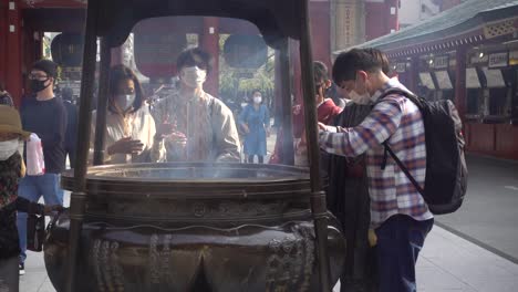 People-wearing-facemask-while-cleansing-themselves-with-smoke-at-Senso-Ji-in-Japan