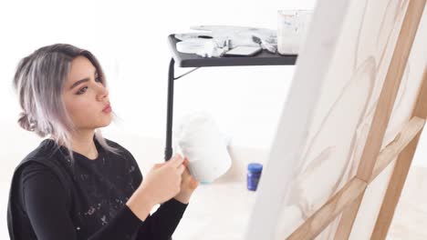 Latina-Artist-In-A-Messy-Look-Working-On-Painting-Canvas-And-Check-Her-Smartphone