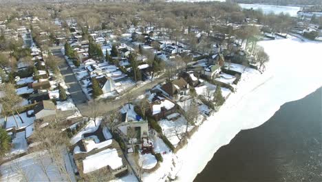 Luftdrohne-über-Schneebedeckten-Häusern,-Wohngebiet-Am-Flussufer