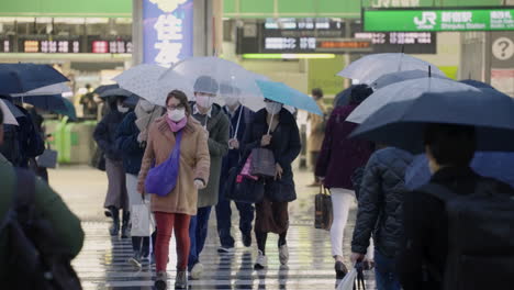 Menschen-Mit-Gesichtsmaske-überqueren-Die-Straße-Bei-Schneefall-Und-Regen-Vor-Dem-Shinjuku-Bahnhof,-Inmitten-Des-Ausnahmezustands-Aufgrund-Der-Covid-19-Pandemie-In-Tokio,-Japan