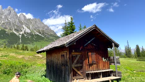 Old-Wooden-Mountain-hiker-house-in-idyllic-landscape-of-Austria-during-sunlight---Woman-hiking-for-break-in-old-cottage