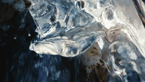 drop-falling-on-icicle-in-a-frozen-river-in-winter-with-flowing-water,-close-up,-slow-motion