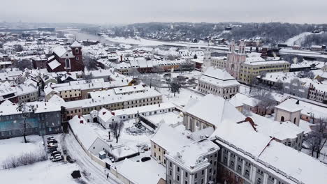 White-snow-covered-rooftops-of-Kaunas-old-town-during-snowfall,-aerial-drone-view