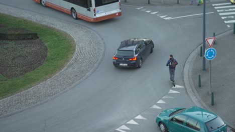 Man-riding-with-an-electric-scooter-enforces-his-place-at-the-roundabout-in-the-city-traffic,-top-down-shot
