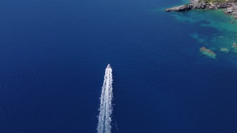 Aerial:-speed-boat-rushing-over-blue-sea-water-near-island-at-Lefkada,-Greece---drone-flying-tracking-shot