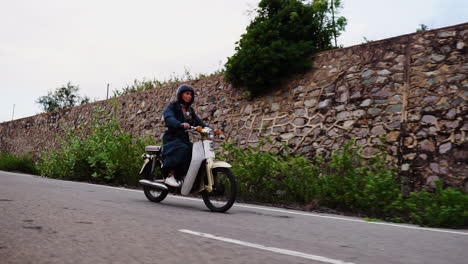 Junge-Kaukasische-Frau-Mit-Mantel-Fährt-Auf-Einem-Weißen-Moped-Motorroller-Auf-Einer-Landstraße
