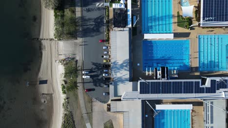 Unique-view-looking-down-at-an-Olympic-pool-complex-built-next-to-a-coastal-city-pathway