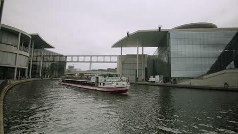 Static-shot-of-Sightseeing-ship-moving-on-spree-river-canal-at-marie-elisabeth-lueders-haus-in-Berlin,-Germany