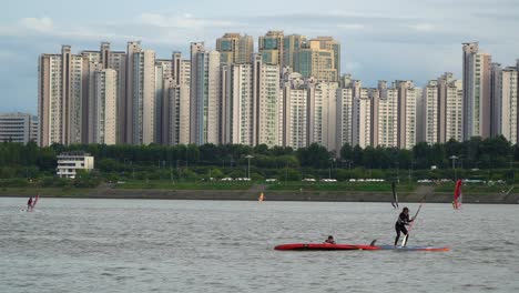Surfer-Falls-Off-The-Paddle-Board-At-Han-River-With-Skyscrapers-In-Background-In-Seoul,-South-Korea
