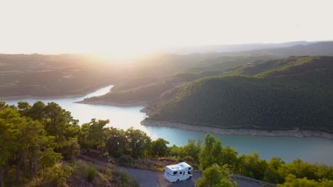Drone-flying-forwards-revealing-a-caravan-parked-with-incredible-views-of-a-blue-and-turquoise-lake-surrounded-by-dense-green-forest