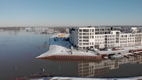 Noorderhaven-aerial-pan-and-reveal-of-contemporary-new-luxury-apartment-building-in-bright-snow-cityscape-mirrored-in-the-high-water-level-in-the-recreational-port-in-the-foreground