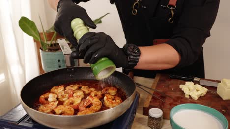 A-professional-chef-wearing-black-gloves,-seasoning-the-shrimps-with-salt,-adding-flavours-and-umami-to-the-delicious-paprika-seafood-dish