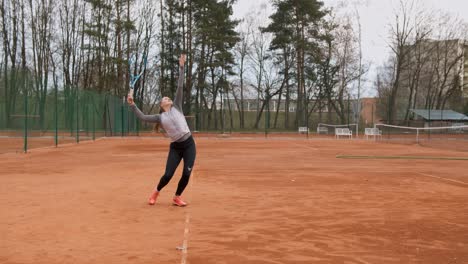Professional-young-female-tennis-player-trains-serve-on-tennis-field-outdoors,static-medium-shot