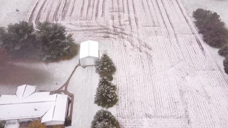 Slow-motion-top-view-of-the-Snowy-Farmland-in-Southeast-Michigan-with-building,-trees-and-land-frozen-in-snow-in-USA