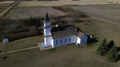 Drone-approaching-beautiful-old-heritage-church-sitting-secluded-in-north-American-prairie-landscape-on-a-sunny-autumn-afternoon