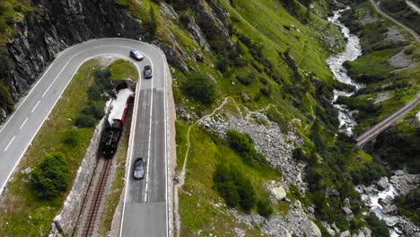 Aerial:-steam-train-leaving-the-tunnel-an-running-along-a-winding-road