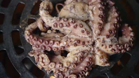 Cinematic-top-down-rotating-shot-of-an-octopus-being-cooked-over-an-open-flame-barbeque-grill-with-fiery-fire-burning-capturing-all-the-fine-details-of-suction-cups-on-the-octopus-tentacles